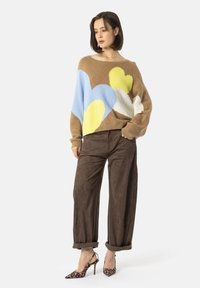 Brun strikket genser med overdimensjonerte hjerte-mønstre i blått, gult og hvitt. Kombinert med løse brune bukser og leopardmønstrede hæler.