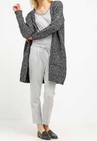 Grå stickad cardigan med en lös passform, bärs över en ljusgrå toppen och matchas med skräddarsydda ljusgrå byxor. Svarta loafers fulländar outfiten.