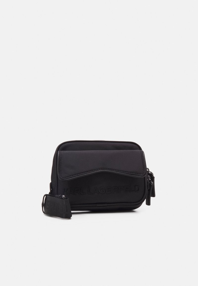 Sac bandoulière en nylon noir avec un rabat avant texturé, fermeture à glissière et logo embossé. Comprend une sangle réglable et un design minimaliste.