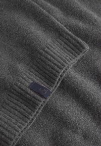Maglione grigio scuro in morbida lana, con texture a costine e un piccolo etichetta blu navy con un logo. Tessuto liscio e caldo con un aspetto accogliente.