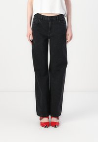 Black denim jeans with a loose fit, featuring small sparkling details throughout. Tapered leg design and five-pocket style, worn with red shoes.