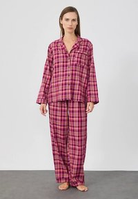 Conjunto de pijama xadrez rosa e roxo, composto por uma camisa com botões e mangas compridas, e calças largas combinando, feitas de tecido macio.