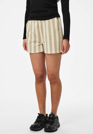 Shorts beige et blancs à rayures, fabriqués en tissu doux avec une coupe décontractée, équipés de poches latérales et d'une taille élastique. Portés avec des baskets noires.