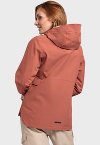 Veste à coque souple de couleur corail, avec une capuche, une coupe ajustée et des poches latérales zippées, au toucher lisse et résistant à l'eau.