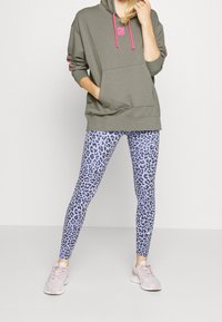 Sweat-shirt vert avec des accents roses et une poche avant, associé à des leggings à imprimé léopard bleu et des baskets rose clair.