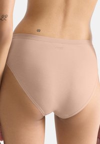 Slip in cotone beige con texture liscia, design a vita alta e dettaglio del logo. La vista posteriore mette in mostra un taglio aderente e bordi senza cuciture.