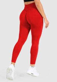 Rote hochtaillierte Leggings mit einem strukturierten Muster, figurbetontem Design und nahtlosen Details, kombiniert mit weißen Sportschuhen.
