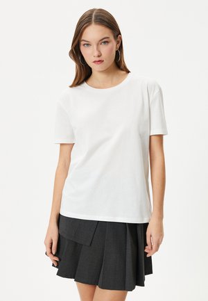 Hvid bomulds t-shirt med korte ærmer og rund hals, kombineret med en mørk plisseret nederdel med lagdelt design.