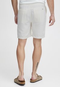 Lysfarvede, knælange shorts lavet af blødt stof, med elastisk talje og to baglommer. Båret med brune slip-on sandaler.