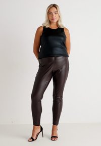 Black sleeveless top with a smooth texture paired with form-fitting brown faux leather pants and black high-heeled sandals.