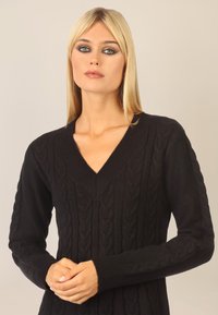 Czarny sweter dziany z dekoltem w kształcie V i długimi rękawami, z teksturowanym wzorem w warkocze oraz ściągaczami przy mankietach i dekolcie.