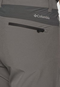 Harmaat ulkovaatteet, joissa on sileä pinta, joustava vyötärö ja musta vetoketjullinen tasku takana, Columbia-logo.