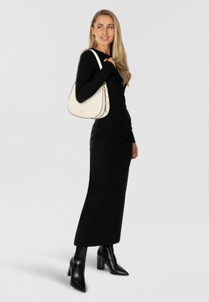 Vestido negro de manga larga y botas de tacón alto negras hasta la rodilla. Bolso blanco de hombro con acentos dorados y ribetes negros. La modelo posa con el cabello suelto.