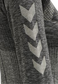 Sudadera deportiva gris con tejido texturizado, que presenta rayas en chevron blancas en contraste y un acento estampado en el hombro.