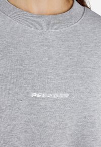 Svetlošedý sveter s textúrovaným, rebrovaným golierom a vyšitým logom "PEGADOR" v bielej farbe na prednej strane. Jednoduchý, neformálny dizajn.