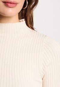 Top a collo alto in crema con coste, caratterizzato da strisce verticali e una finitura testurizzata, con collo alto e design aderente.