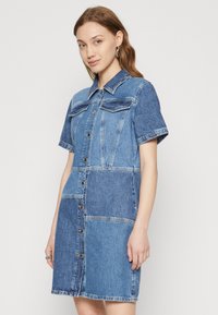 Denim srajčna obleka s patchwork dizajnom v različnih odtenkih modre, kratkimi rokavi, ovratnikom in sprednjim gumbom.