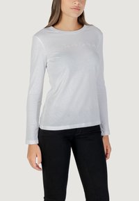 T-shirt bianca a maniche lunghe con scollatura tonda, texture morbida, caratterizzata da un discreto ricamo del marchio sul petto e un orlo dritto.