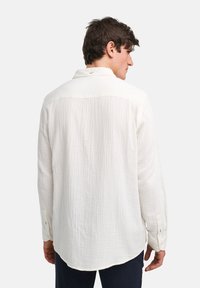 Witte lange mouwen shirt met een textured stof, subtiel ruitpatroon, knopenmanchetten en een klassieke kraag, weergegeven vanuit een achteraanzicht.