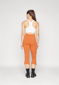 Sutiã atlético branco e calças justas laranja com comprimento até a metade da panturrilha, apresentando um design ajustado, usadas com meias pretas e ténis.