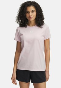 Camiseta de algodón rosa claro con cuello redondo, mangas cortas y un pequeño logotipo blanco en el pecho. Combinada con pantalones cortos negros.