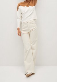 Il maglione accorciato presenta un design a blocchi di colore marrone e bianco, abbinato a jeans a gamba larga color crema e scarpe color cammello.