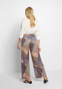 Kalhoty s širokými nohavicemi, které mají geometrický vzor v odstínech modré, růžové a béžové. Vyrobeno z lehkého materiálu s elastickým pasem.