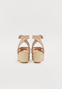 Sandale tip wedge din piele tan, cu curele textile intersectate și toc din jute țesut. Designul include o închidere cu cataramă și o suprafață texturată a tocului.