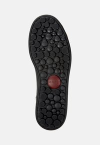 Musta kumipohja, jossa on teksturoitu kuvio pyöreistä nyppylöistä, punaisella pyöreällä korostuksella, jossa on sana "camper" ja koko "42".