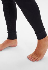 Black cotton leggings with a fitted design, featuring ribbed cuffs at the ankles. Bare feet visible on a light background.