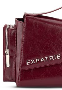 Burgundská kabelka z faux kože so štruktúrovaným tvarom, striebornými kovovými doplnkami, zipsovou kapsou a embosovaným logom na prednej strane.