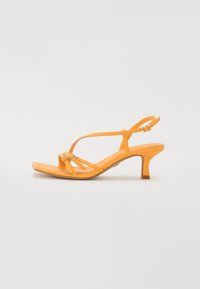 Sandale en cuir orange à lanières avec un bout carré, une fine bride de cheville et un petit talon carré. Présente des boucles métalliques subtiles et une texture lisse.