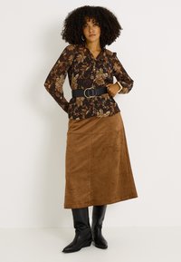Falda maxi de ante marrón combinada con una blusa negra de flores con mangas largas y cintura ajustada, complementada con un cinturón ancho negro.