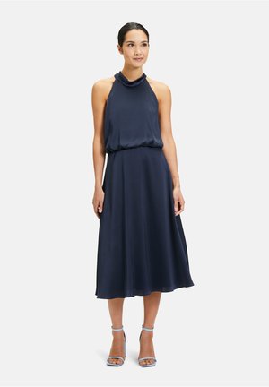 Marineblaues ärmelloses Kleid mit Kragen, geraffter Taille und fließendem Rock. Glattes Material mit einem subtilen Glanz. Kombiniert mit hellblauen Absatzsandalen.