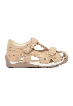 Beige Kindersandale mit Herzmustern, zwei verstellbaren Klettverschlüssen, offenem Zehen- und Fersenbereich und flexibler brauner Sohle.