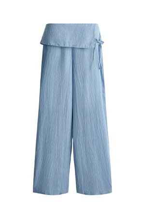 Personne portant un pantalon côtelé bleu clair taille haute avec un cache-cœur à l'avant et un détail nœud, associé à une chemise blanche à manches courtes.