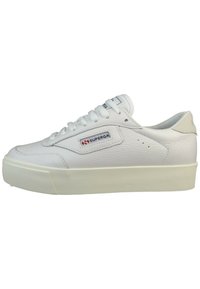 White leather sneaker with a textured surface, round toe, flat white laces, and a stacked rubber sole. Features a red and blue logo patch.