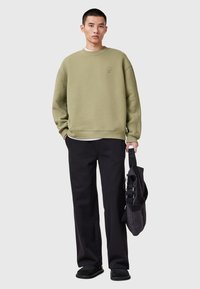 Sudadera verde oliva con puños y dobladillo acanalados, combinada con pantalones negros y un bolso negro. Textura suave, corte relajado, branding mínimo.