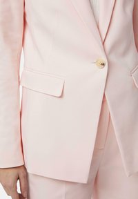 Blazer rosa chiaro, design sartoriale, chiusura a un bottone, rever a nicchia, due tasche frontali, texture liscia.