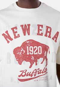 T-shirt blanc en coton avec un graphisme de buffle rouge et le texte "NEW ERA 1920" en lettres grasses et usées.