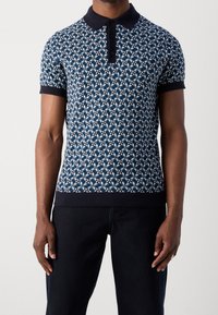 Koszulka polo z krótkim rękawem, charakteryzująca się wzorem geometrycznym w kolorze granatowo-białym, z jednolitym granatowym kołnierzykiem i mankietami oraz zapięciem na guziki.