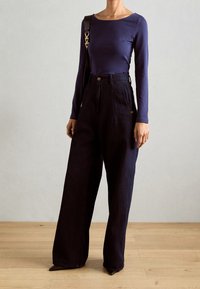 Haut à manches longues bleu marine associé à un pantalon large taille haute de couleur sombre. Le haut a un col rond ; le pantalon est équipé de poches latérales et d'une fermeture à bouton.