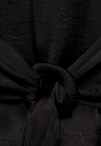 Tissu noir à texture douce, présentant un détail de design noué au centre et des sections fluides de chaque côté.