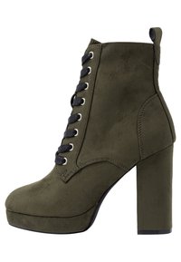 Botte au cheville en suède vert olive avec un chunky talon haut, bout rond et lacets noirs passés dans des œillets en argent. Présente une languette à l'arrière.