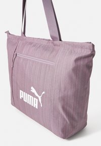 Lila gestreifte Tragetasche aus Stoff. Verfügt über eine Reißverschlusstasche auf der Vorderseite und ein weißes Puma-Logo an der unteren Vorderseite. Lange Tragehenkel sind ebenfalls enthalten.