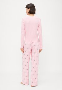 Camisola de manga longa rosa clara e calças de pijama. As calças apresentam um padrão repetido de "Rainha do Sono" e pequenos desenhos de coroas. Tecido macio.