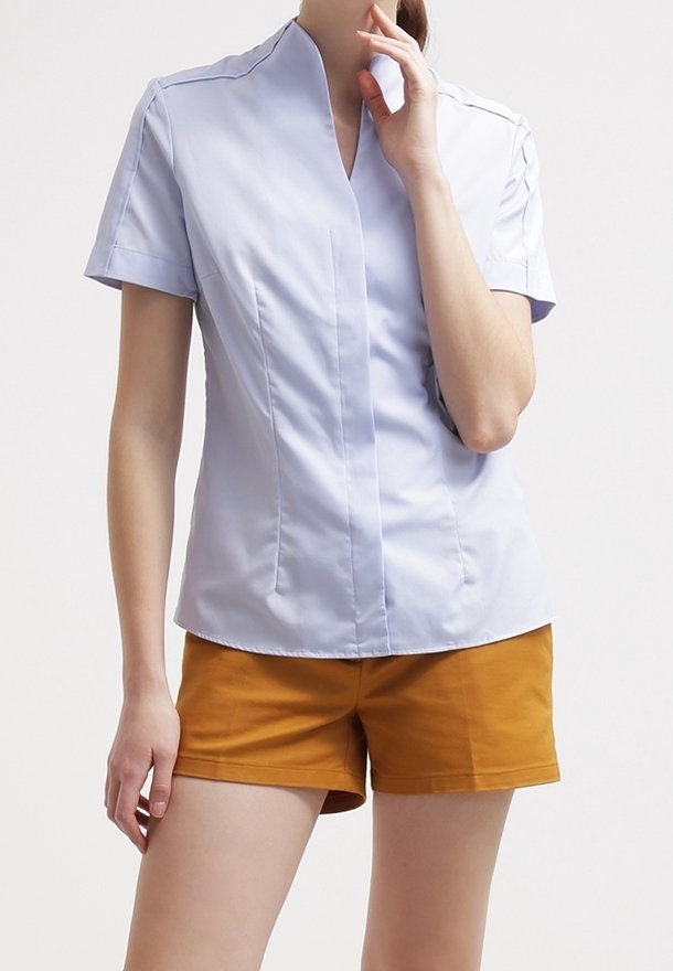 Chemise bleu clair à manches courtes avec un décolleté en V, dotée de coutures angulaires et d'un tissu lisse, associée à un short de couleur moutarde.