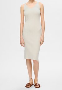 Robe midi en maille beige clair, avec un col en V, une coupe ajustée et une texture côtelée. Associée à des sandales à enfiler marron.