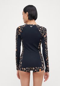Long-sleeve rash guard in black with colorful floral prints on sleeves and sides, made of stretchable fabric, designed for water activities.
