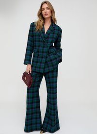 Zweiteiliger Plaid-Anzug in Dunkelgrün, Blau und Schwarz. Besteht aus einer zweireihigen Jacke und ausgestellten Hosen. Akzentuiert mit einer burgunderfarbenen Handtasche.